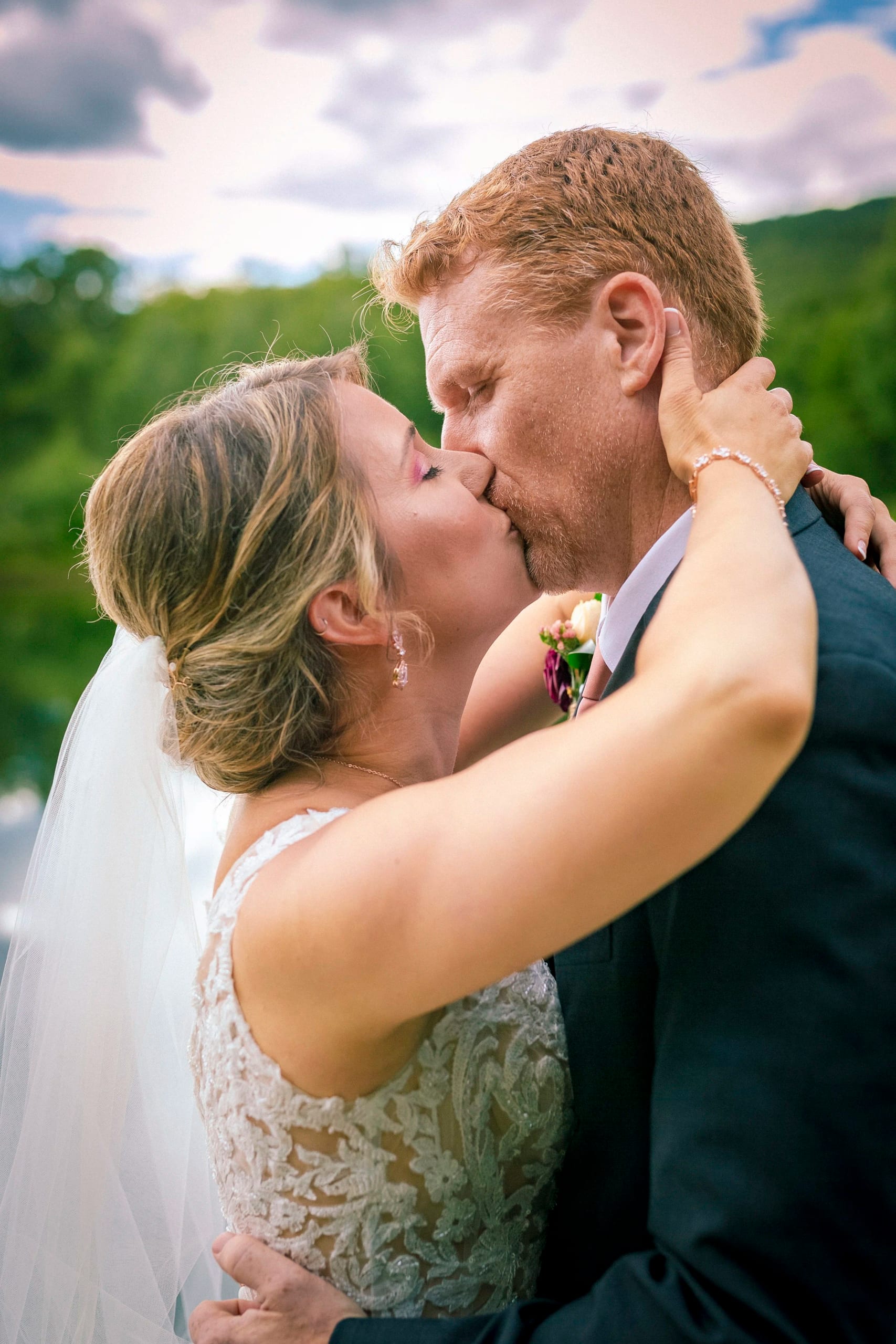 A bride and groom kiss outdoors with green hills behind them