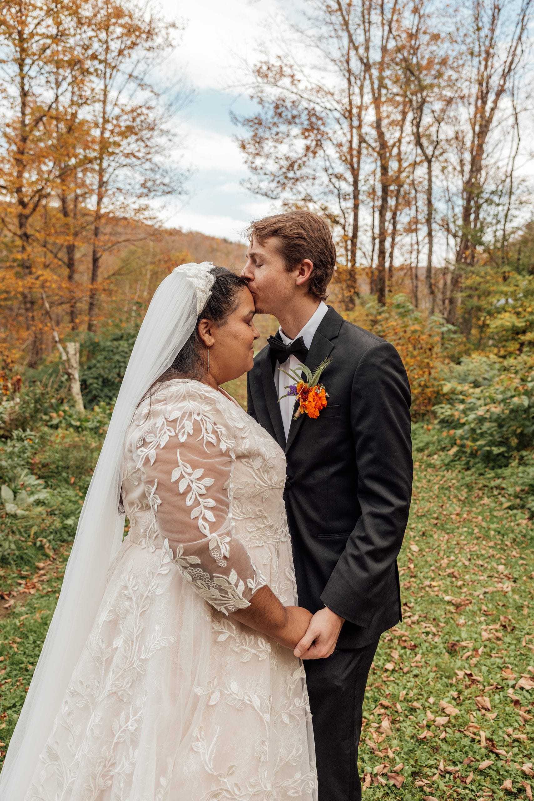 A groom kisses his bride on the forehead in an autumn field