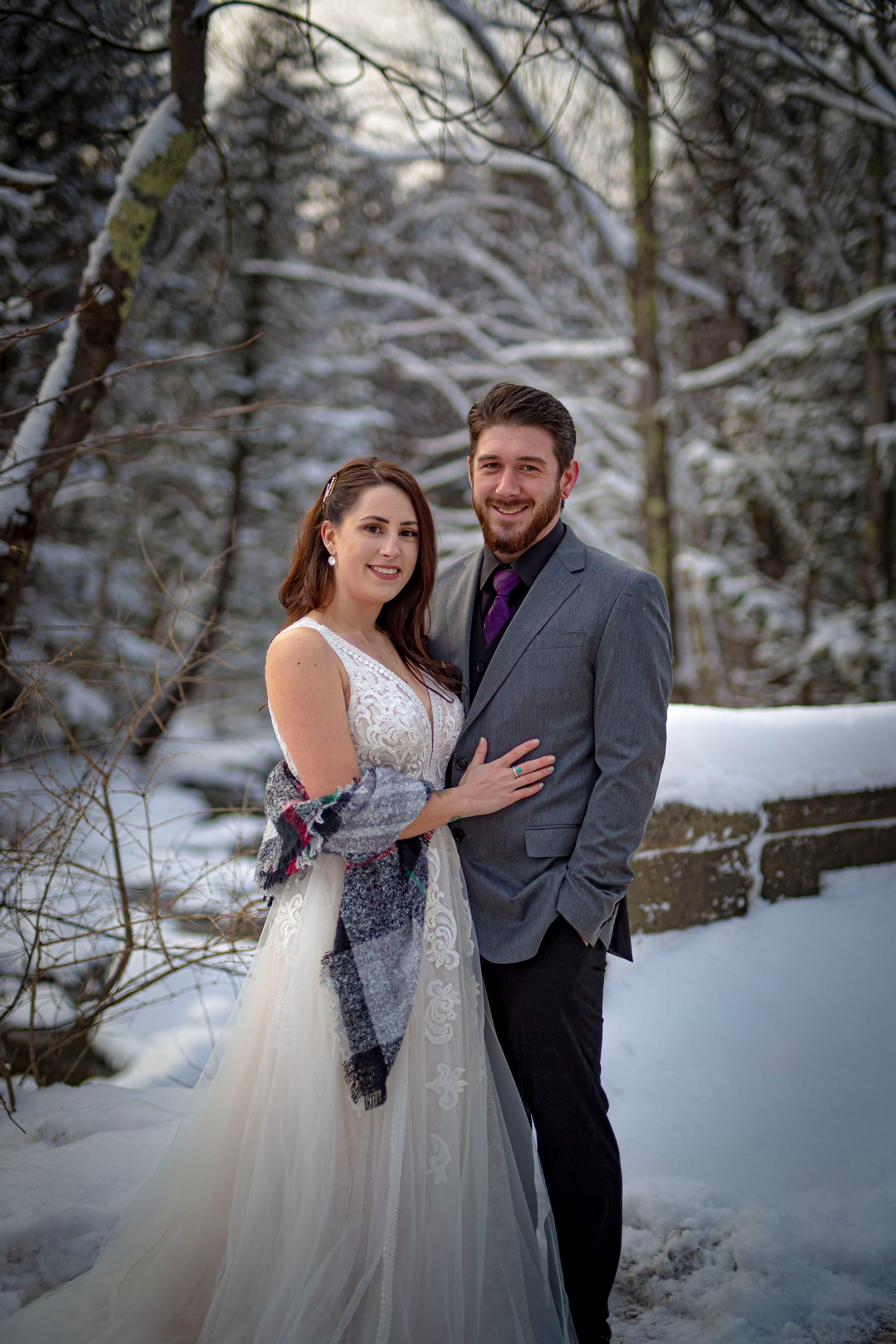 A bride and groom embrace in a snowy forest