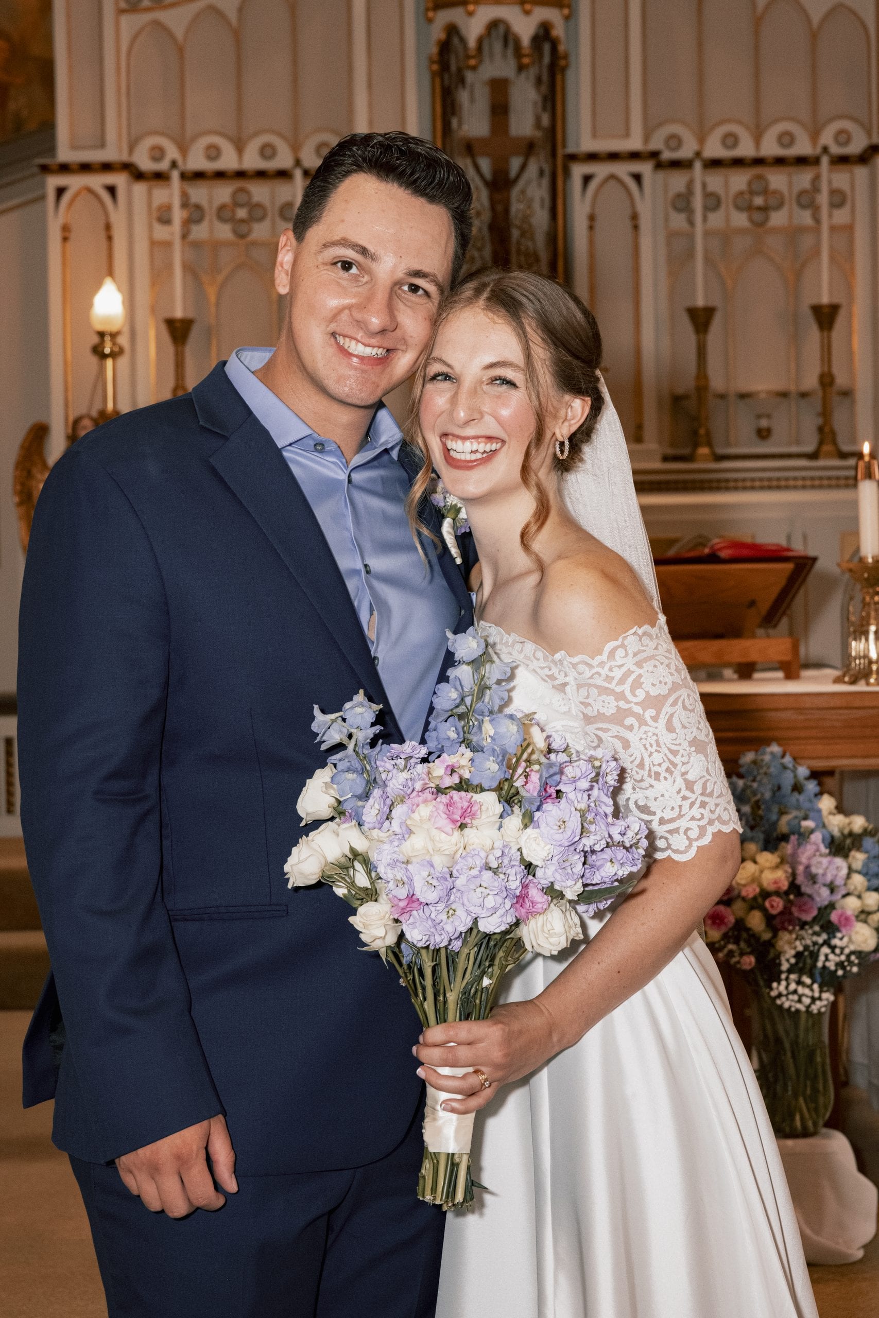 A smiling bride and groom pose close together beside the church altar