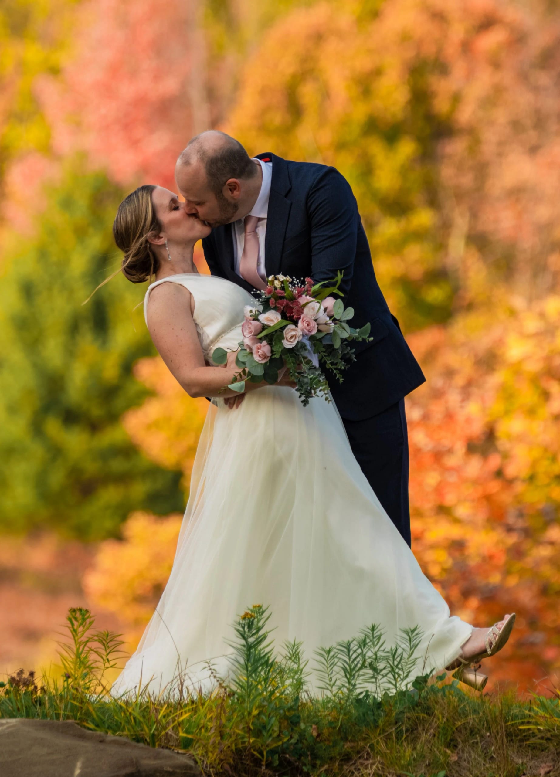 A groom dips his bride for a kiss among bright autumn leaves